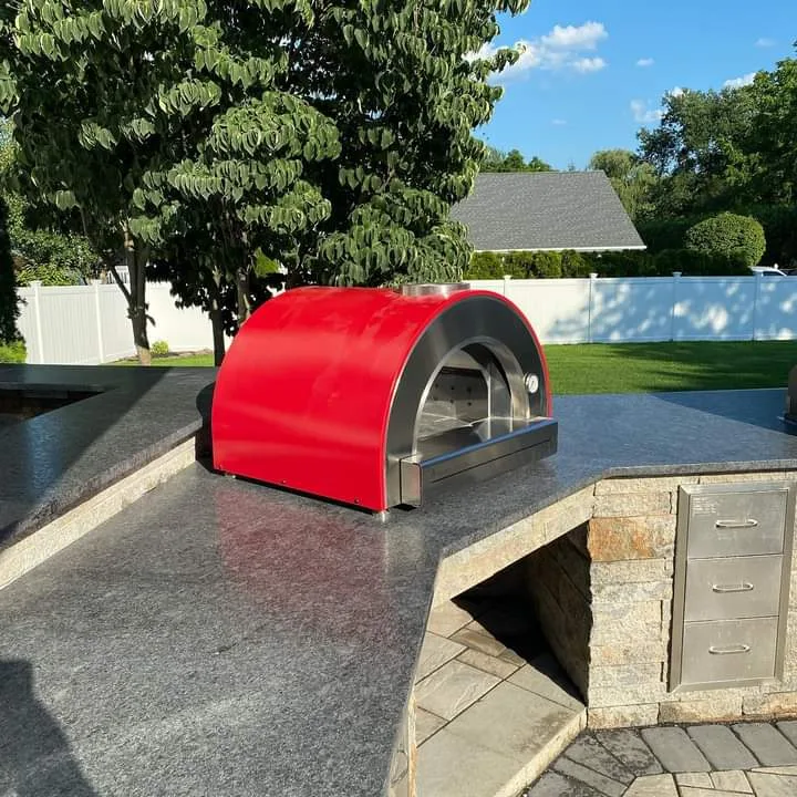 Granite outdoor kitchen counter with a red pizza oven and stacked-stone base