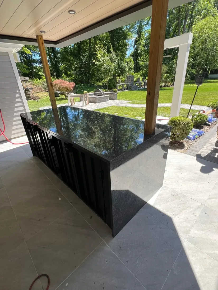 Polished black granite outdoor kitchen island under a covered patio in a Newark, NJ backyard