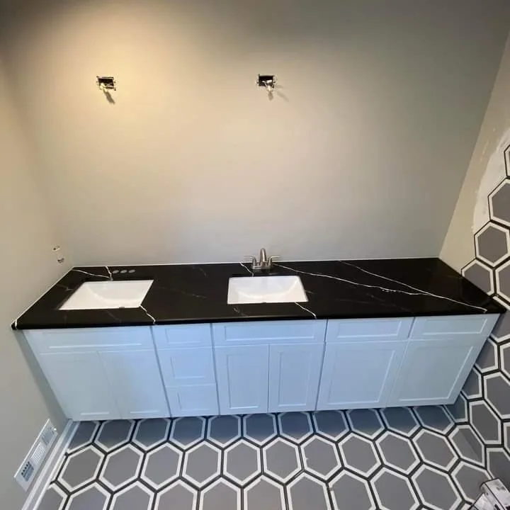 Black marble double-sink bathroom vanity with white cabinets over hexagon tile flooring