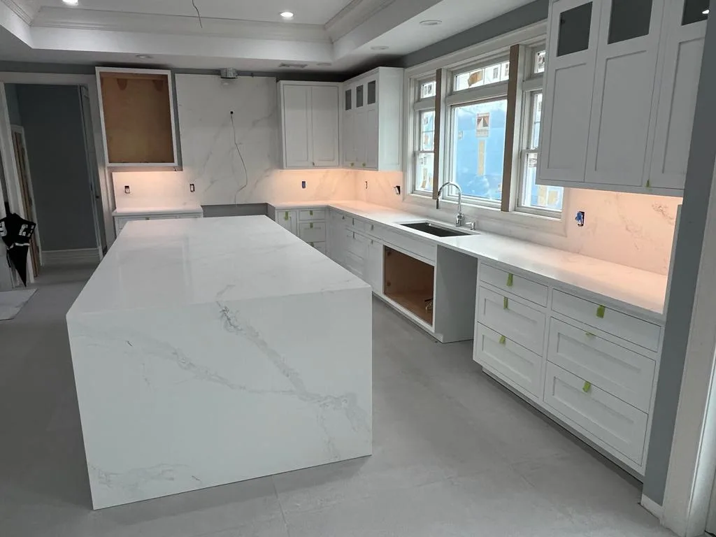 Large porcelain-marble waterfall island in a bright kitchen with white shaker cabinets