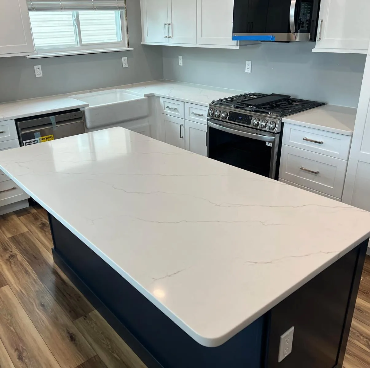 Calacatta quartz kitchen island on a navy base with a farmhouse sink and white cabinetry